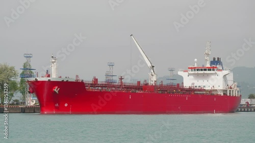 Red oil tanker moored in industrial harbor used for maritime logistics, energy export, crude oil shipping, international trade and global cargo transportation industry