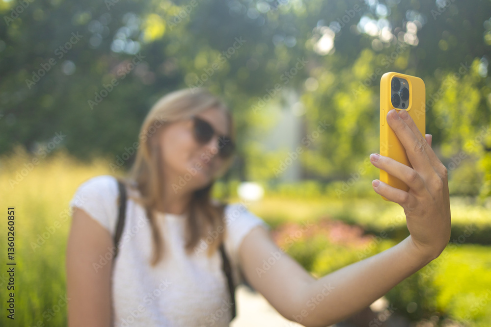 Stylish smiling 30s lady taking selfie outdoors in city park, happy young female capturing self-portrait while enjoying walk and good day, resting outside