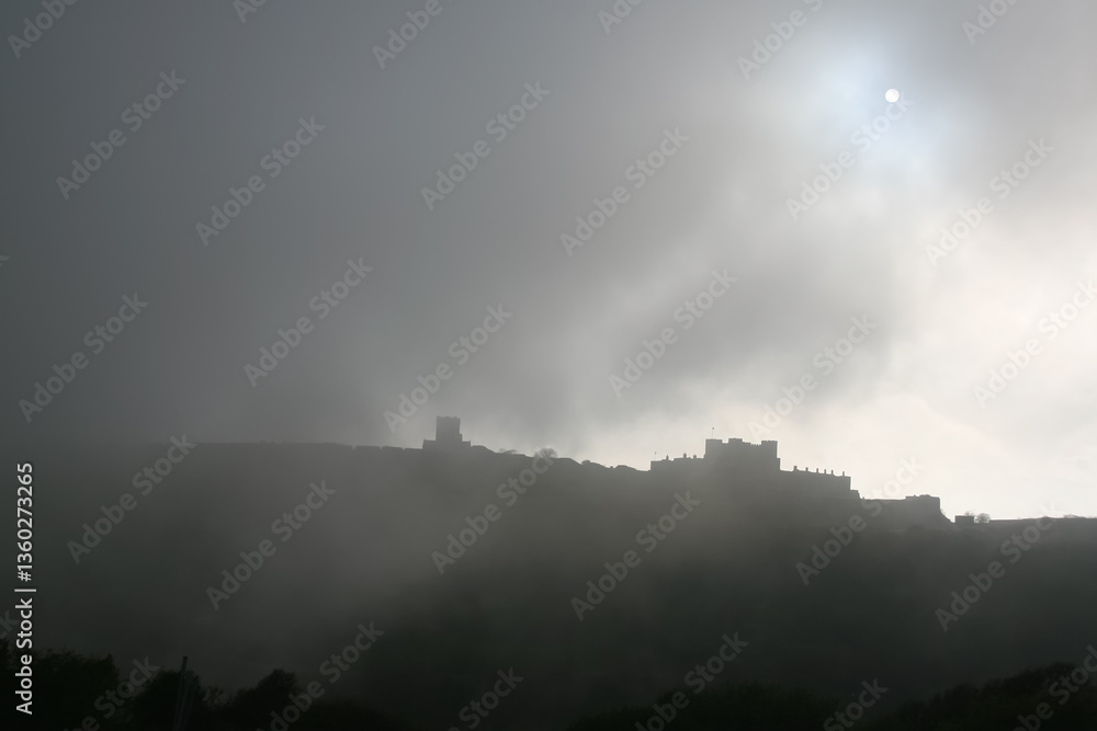 Sun visible through clouds and fog over silhouette of Dover castle