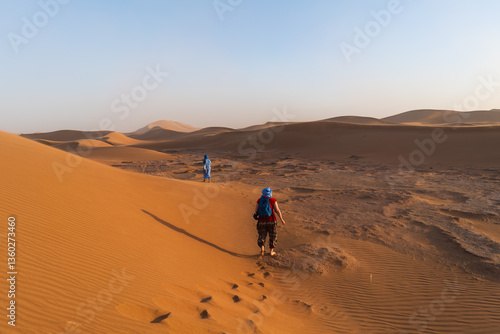 Two people trekking travel through the Sahara Desert amidst sand dunes and arid landscape