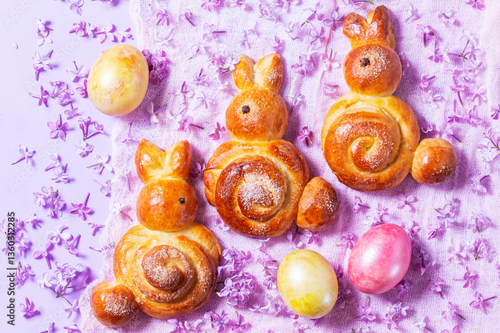 Easter composition made of sweet buns in the shape of a rabbit, eggs and lilacs.