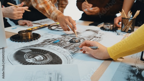 A group of engineers engaged in a creative workshop, actively analyzing detailed technical drawings related to machinery and mechanical components with various tools. SACTR