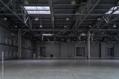 Industrial interior expanse, expansive space under a metal beam framework roof illuminated by numerous lights and skylights