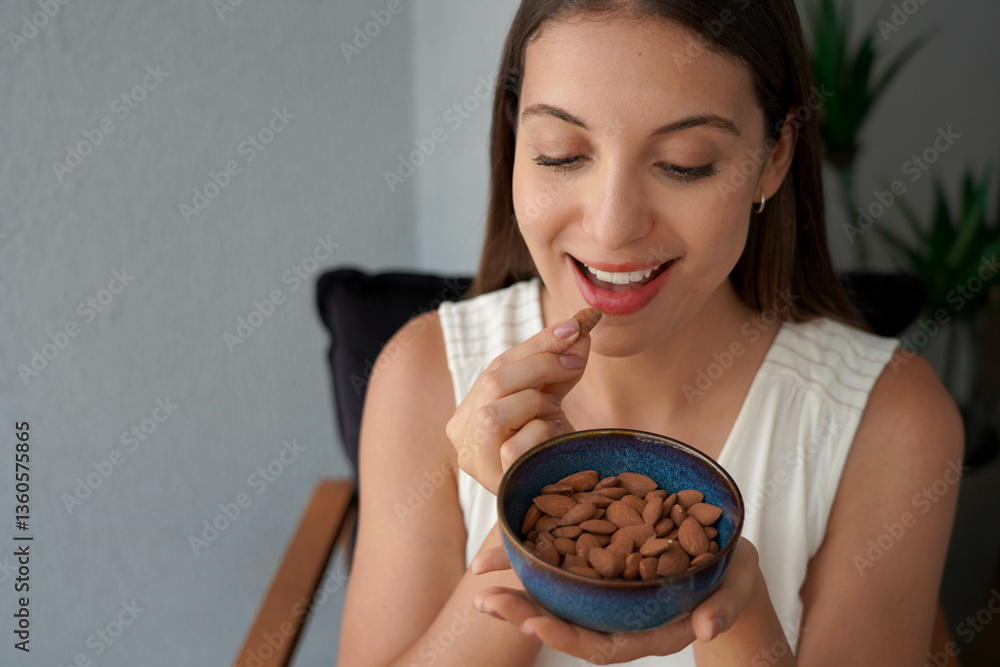 Beautiful healthy young woman eating almonds unpeeled as snack at home. Looking down. Copy space.
