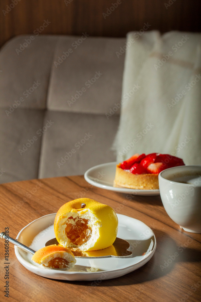 Mousse cake with peach filling covered with velvet glaze and a cup of latte on a table in a cafe.