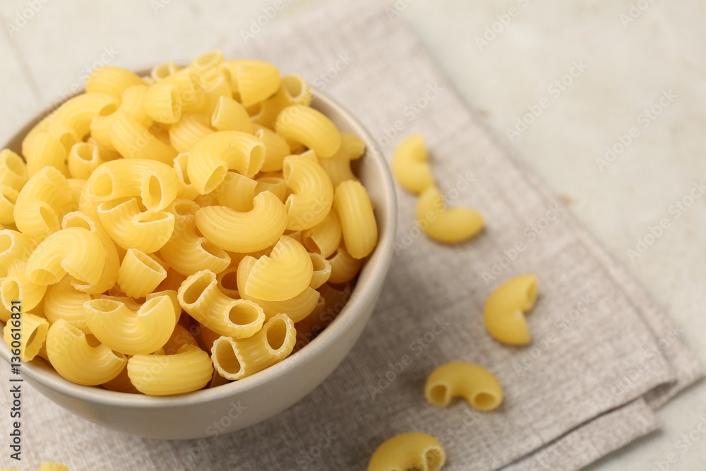 Raw horns pasta in bowl on gray table, closeup. Space for text Raw horns pasta in bowl on gray table, closeup. Space for text