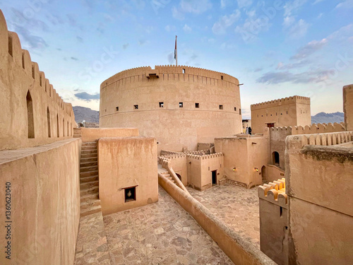 Nizwa Fort, Oman - Ancient circular fortification with crenellated walls and towers under a cloudy sky, showcasing the rich history and architectural heritage of Oman