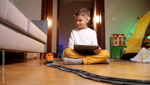 Young boy is using a tablet while sitting on the floor of a playroom, surrounded by toys, seemingly more interested in the digital world