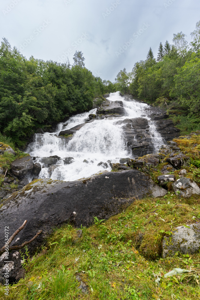 Obraz premium Holebroa waterfall over Geiranger village in More og Romsdal county, in Stranda municipality western Norway surrounded by unspoiled lush