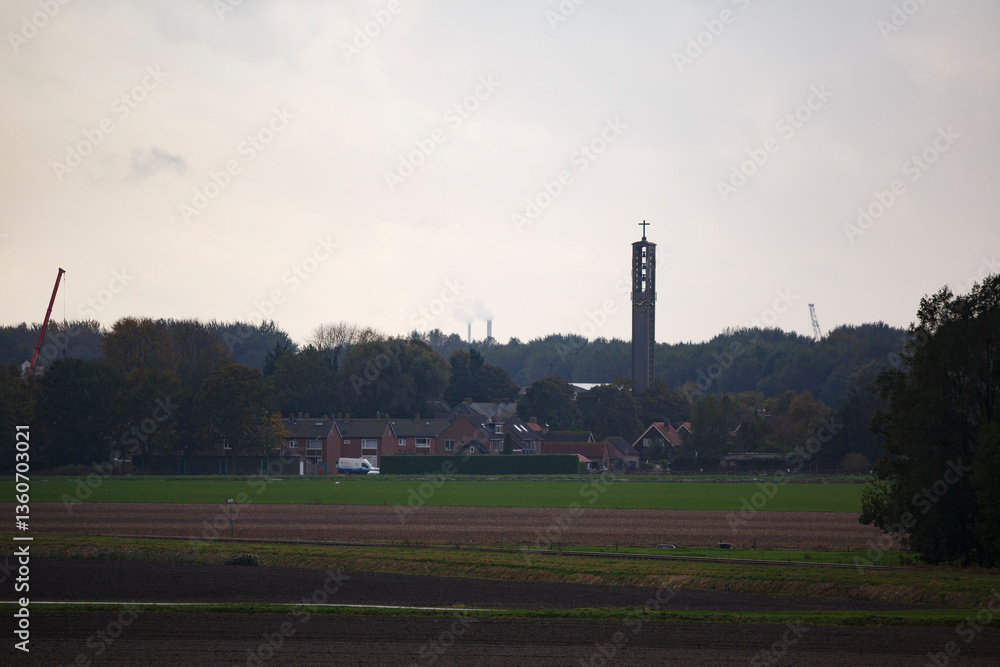 Obraz premium View of a countryside village with a church tower and smoke stacks on a cloudy day