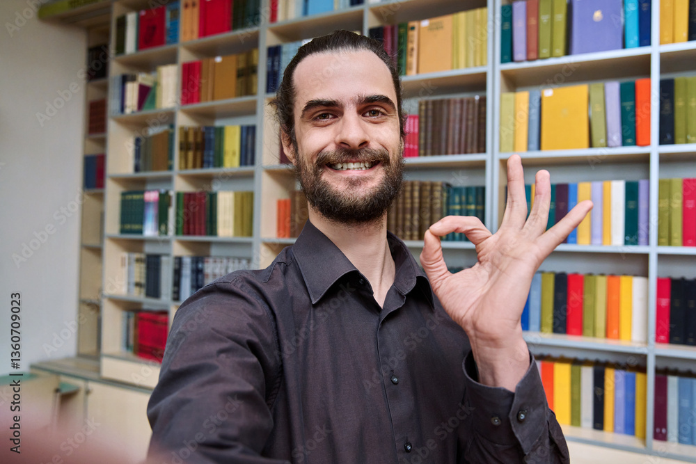 Selfie photo portrait young 30s positive man inside library showing ok gesture