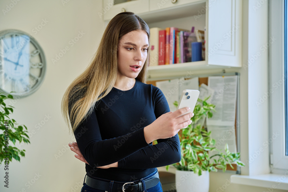 Young surprised woman using smartphone standing at home Young surprised woman using smartphone standing at home