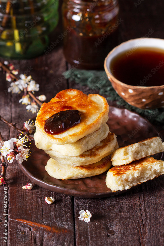 Lenten yeast pancakes with plum jam and tea, and a bouquet of blooming apricot branches on a wooden table.
