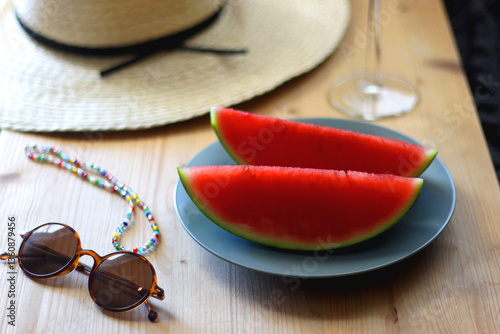 Obraz na płótnie Plate with watermelon slices, glass of orange juice or cocktail, straw hat, colorful beaded necklace and sunglasses on the wooden table. Summer essentials concept. Selective focus. w salonie