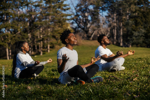 Фотография Group of three black yogi sportspeople in lotus position meditating in nature