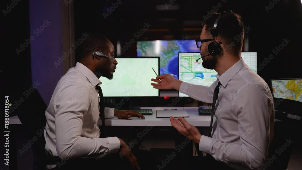 Two logistics dispatchers in a control center analyze maps and discuss freight transportation routes Two logistics dispatchers in a control center analyze maps and discuss freight transportation routes
