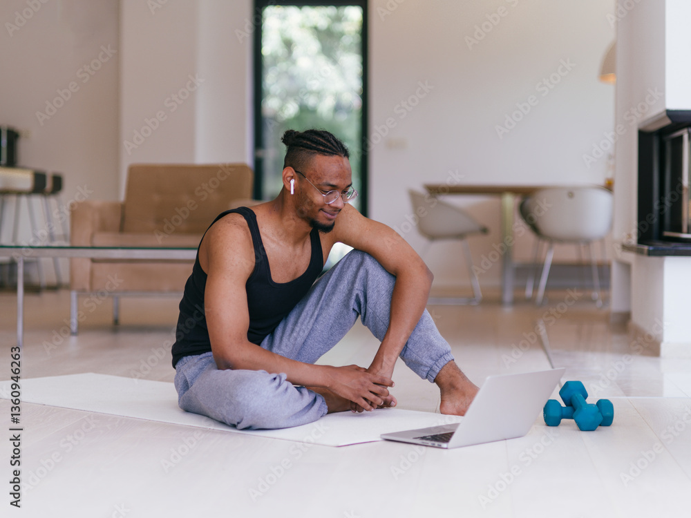 Fototapeta premium Training At Home. Sporty man doing the training while watching an online tutorial on a laptop, exercising in the living room, free space.