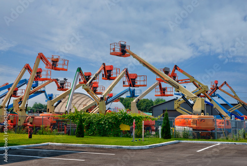 Outdoor lot filled with colorful boom lifts and aerial platforms lined up under a partly cloudy sky, showcasing heavy construction equipment ready for industrial or rental use.
