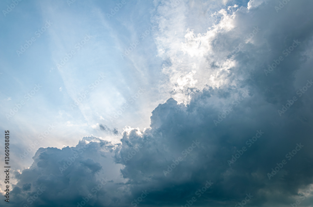 Obraz premium Moody sky with sun rays piercing through thick, dark storm clouds. A powerful atmospheric scene capturing the calm before a summer thunderstorm. Perfect for backgrounds or weather themes.