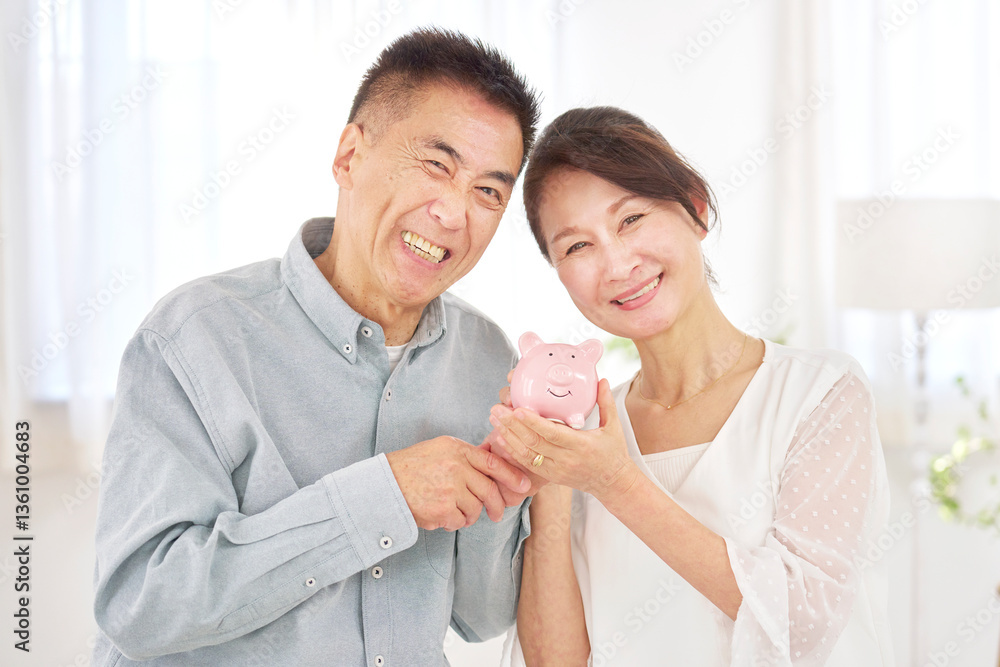 貯金箱を持つシニア夫婦 リビング 貯金箱を持つシニア夫婦 リビング