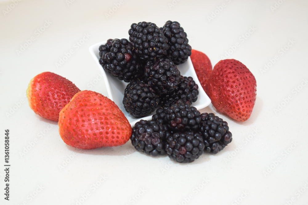 Blackberries spilling out of a white cup accompanied by vibrant strawberries Blackberries spilling out of a white cup accompanied by vibrant strawberries