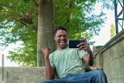 overexcited black man looking at mobile phone horizontally while isolated over nature background 