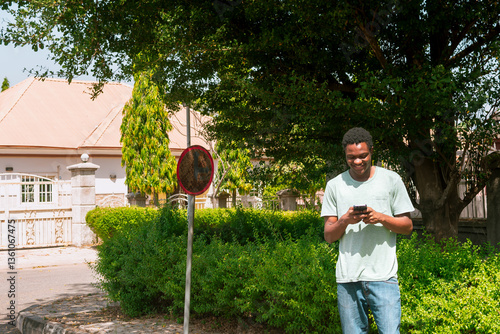 young african man smiling standing using mobile phone while isolated over colorful estate neighborhood 