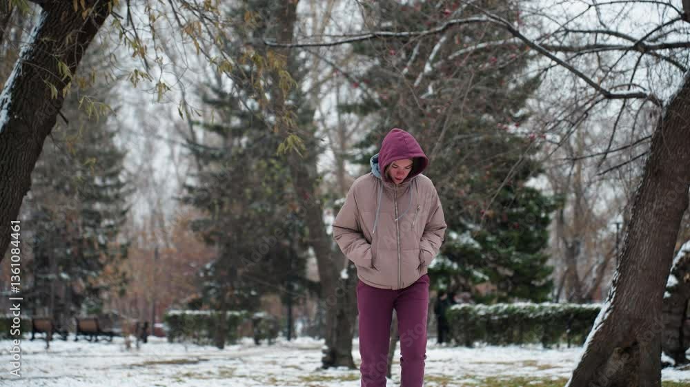 Young girl happily jumps in winter snow park, dressed in warm hoodie and coat, trees covered in snow create a scenic background, while she playfully enjoys cold weather in serene outdoor setting Young girl happily jumps in winter snow park, dressed in warm hoodie and coat, trees covered in snow create a scenic background, while she playfully enjoys cold weather in serene outdoor setting