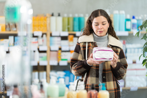 Fotografie Young woman buyer chooses feminine sanitary pads in pharmacy