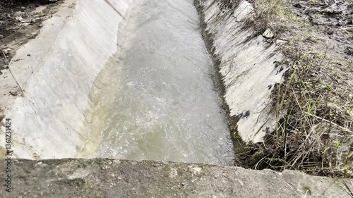 Close-up of a part of an irrigation channel designed for agriculture to transport water from a source to various use. A hiking trail leads along the irrigation canal