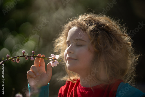 Obraz na płótnie Child face close-up in spring park. Child enjoying spring sunshine. Child smelling flowers spring sunny day. Portrait of kid in blossoming garden. Child fun in spring. Kid with pink blossom flowers. w salonie