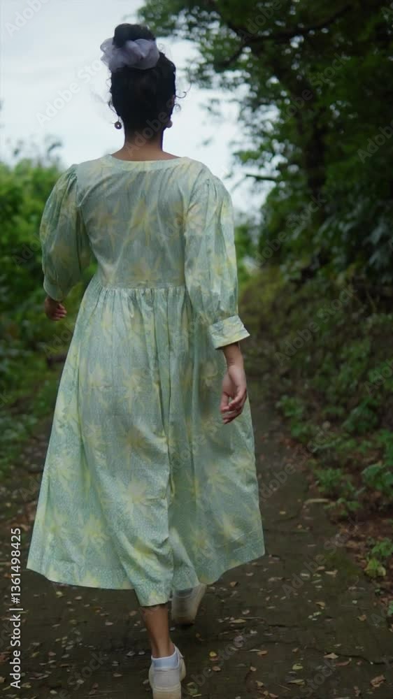 A person walking on a rural path, wearing a flowing dress in nature, India A person walking on a rural path, wearing a flowing dress in nature, India