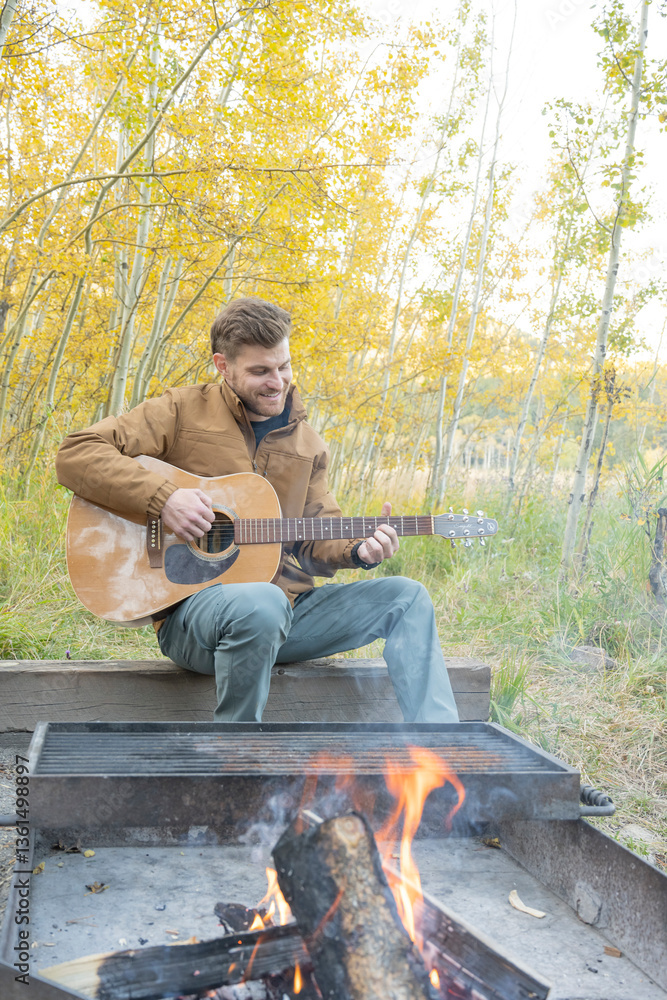 Fototapeta premium Man smiles and plays guitar while camping
