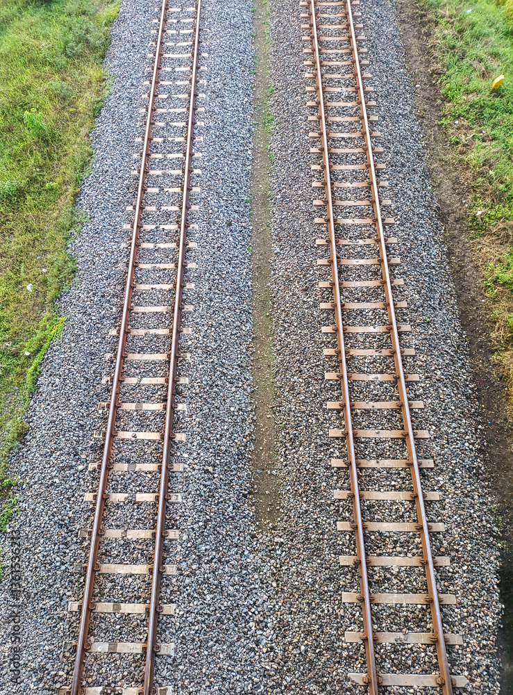 Obraz premium Symmetrical aerial view of dual railway tracks over gravel and surrounded by grassy terrain.