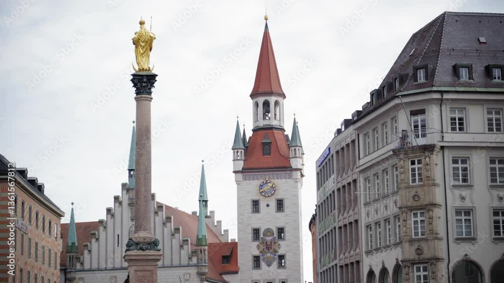 The golden statue of Virgin Mary atop Mariensäule with Munich's Old Town Hall in the background. A historic cityscape at Marienplatz on a cloudy day, showcasing Gothic and Baroque architecture. The golden statue of Virgin Mary atop Mariensäule with Munich's Old Town Hall in the background. A historic cityscape at Marienplatz on a cloudy day, showcasing Gothic and Baroque architecture.