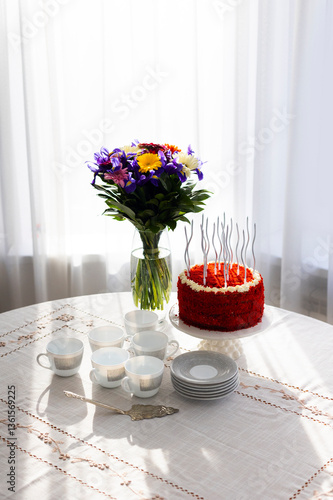 Bithday cake called Red Velvet with twisted silver candles on laid table with porcelain cups, saucers and colorful flower bouquet
