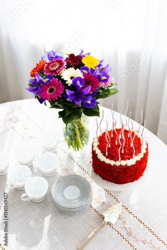 Bithday cake called Red Velvet with twisted silver candles on laid table with porcelain cups, saucers and colorful flower bouquet
