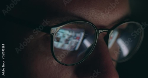 Close up portrait of male in glasses with reflection of computer screen working online. Close up male eyes in eyeglasses working late at night scrolling internet pages in front of laptop computer