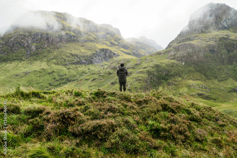 Obraz premium Girl standing in the scottish highlands surrounded by hills in clouds