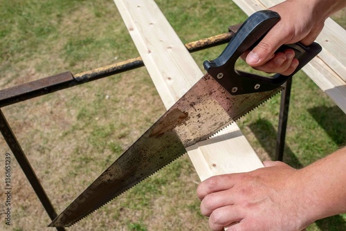 A saw in a man's hand saws a board.