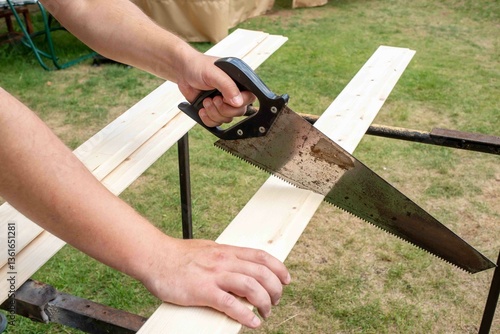 A saw in a man's hand saws a board.