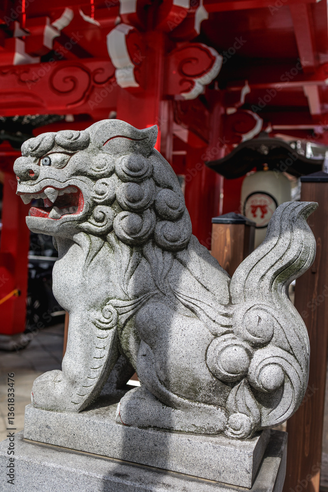 Obraz premium Detailed side view traditional Japanese komainu stone lion statue, guarding the vibrant red orange wooden structure of a buddhist temple's entrance. Stone figure has great cultural significance.