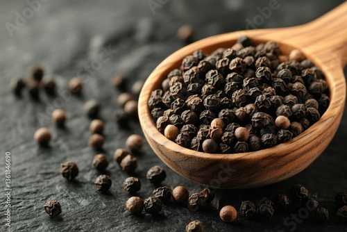 Black peppercorns in a wooden spoon on a dark stone surface arranged artfully for culinary use or spices