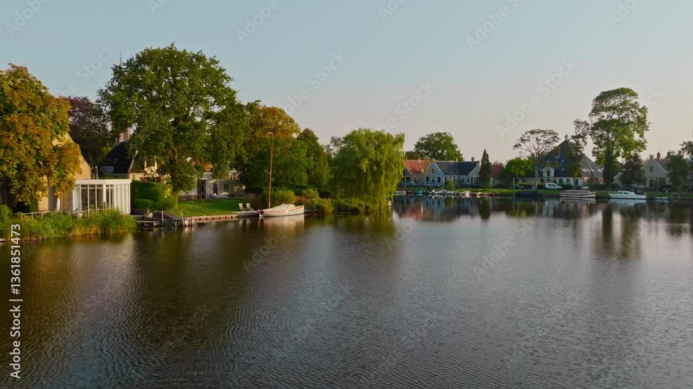 A low drone flight over the water towards a historic church in Broek in Waterland, Netherlands. Captured in 4K on a sunny summer morning, showing wooden houses, meadows, and a peaceful lake A low drone flight over the water towards a historic church in Broek in Waterland, Netherlands. Captured in 4K on a sunny summer morning, showing wooden houses, meadows, and a peaceful lake