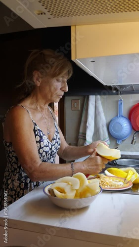 Vertical video: An elderly blonde woman slices a white melon on the kitchen counter, ready to serve a fresh summer fruit.
