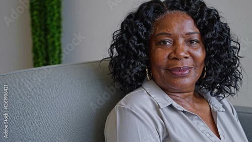 black woman in her 50s sitting in a waiting room sofa, slightly overweight patient, black curly hair