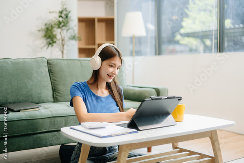 Young asian woman using smartphone and tablet while seated on couch at home