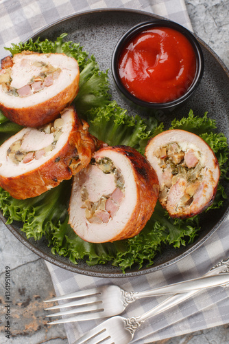 Baked homemade turkey roll with bacon, onions and mushrooms close-up in a plate on the table. Vertical top view from above