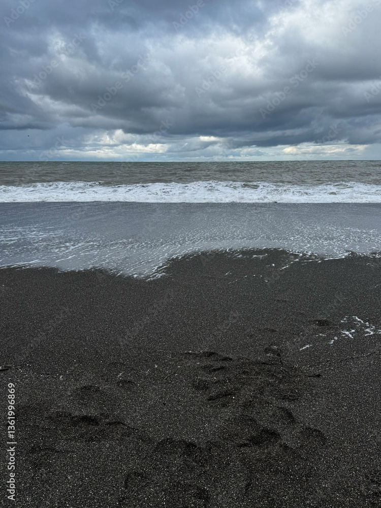 Black sand beach with ocean waves and moody clouds
