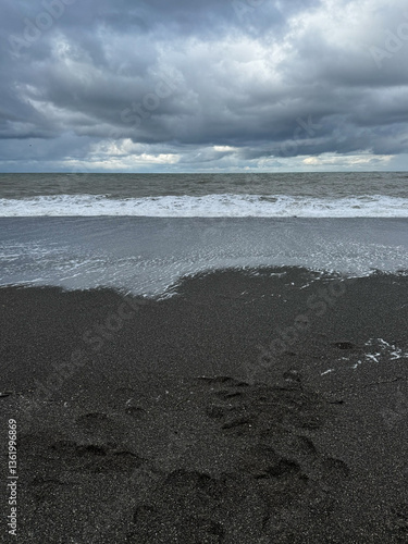 Black sand beach with ocean waves and moody clouds